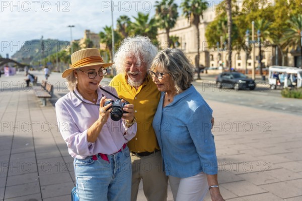 Three happy senior friends are standing on a city street, looking at images on a camera's screen, celebrating their friendship and travel experiences together