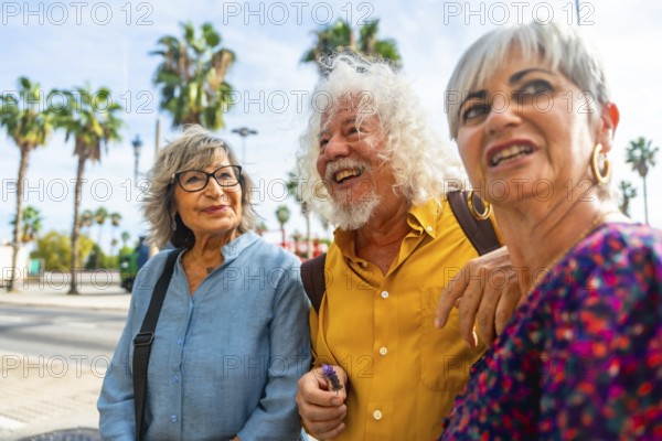 Three happy senior friends enjoying a vacation while walking together on a city street, sharing moments and discussing, with palm trees visible in the background under a clear sky