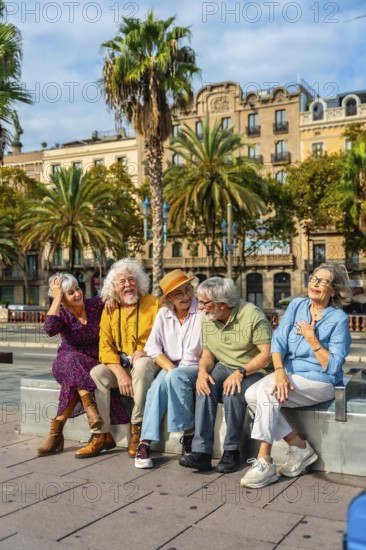 Group of happy senior friends enjoying their city vacation, sitting outdoors and laughing together under the palm trees, celebrating friendship and active retirement