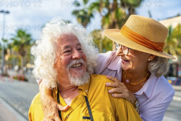 Senior couple embracing and smiling at each other outdoors on a sunny vacation, enjoying retirement, warm weather, palm trees and joyful, affectionate moments together