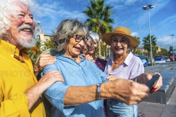 Group of smiling seniors enjoying a vacation, standing outdoors together and using a smartphone to capture a cheerful selfie, reflecting modern retirement and friendship