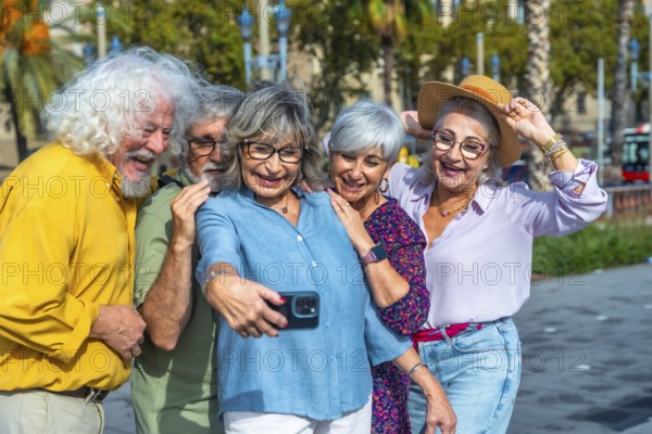 Group of five cheerful seniors enjoying leisure time together, standing close and smiling while capturing a memorable selfie with a mobile phone in an urban park