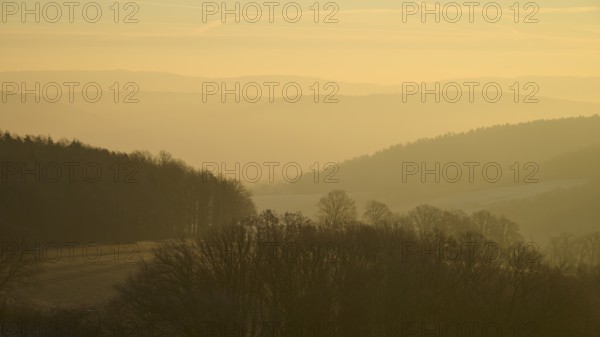 Blurred hills and trees in morning fog with a golden sky at sunrise, Seckmauern, Lützelbach, Maintal, Odenwald, Hesse, Germany