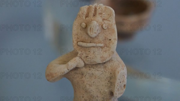 Figurine of a boy holding a mask in front of his face, ancient clay figure with simple facial features and rough texture, Archaeological Museum, Nemea, Peloponnese, Greece