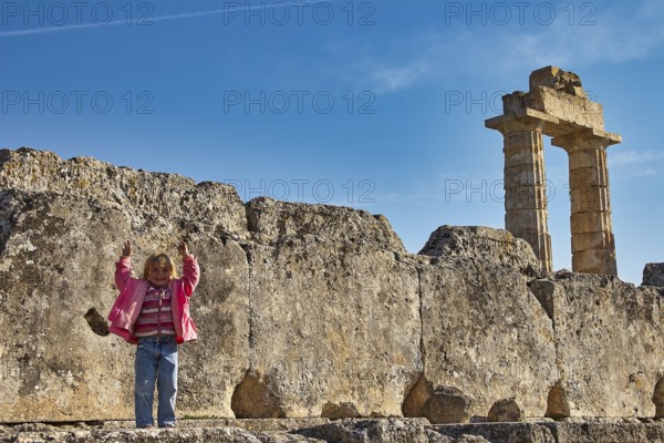 Child standing in front of an ancient column. Stones and sky in the background, Nemea, Ancient Zeus Church, Archeological Site, Peloponnese, Greece