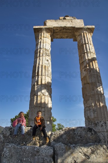 Two children sit in front of an ancient column. Clear Sky, Nemea, Ancient Zeusheightum, Archaeological Site, Peloponnese, Greece