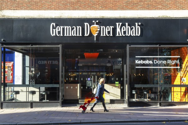 Person passing GDK German Doner Kebab takeaway restaurant in city centre, Exeter, Devon, England, UK