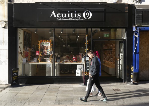 Shoppers passing Acuitis opticians and hearing centre shop store, High Street, Exeter, Devon, England, UK