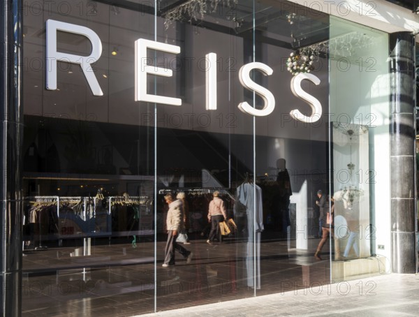 Shoppers walking reflected in Reiss shop store window in city centre, Princesshay, Exeter, Devon, England, UK
