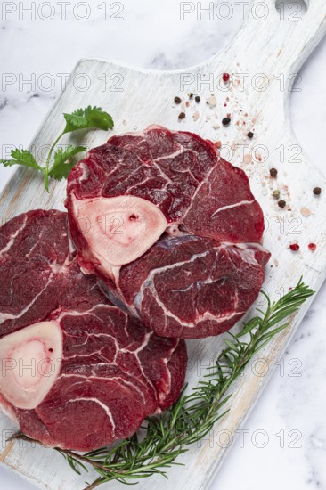Knuckle on the bone, raw meat for ossobuco, on a wooden chopping board, with a sprig of rosemary, and spices, top view, no people