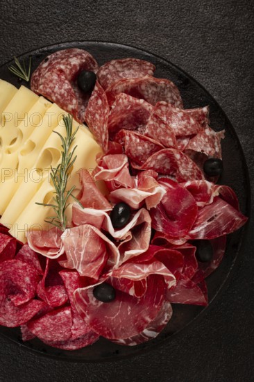 Cold cuts, appetizer, prosciutto, salami and ham, with maasdam cheese and olives, on a round plate, breakfast, top view, close-up, deserted