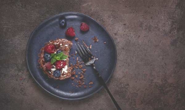 Half-eaten chocolate tartlet, on a plate, stuffed with cottage cheese and berries, breakfast, homemade, no people
