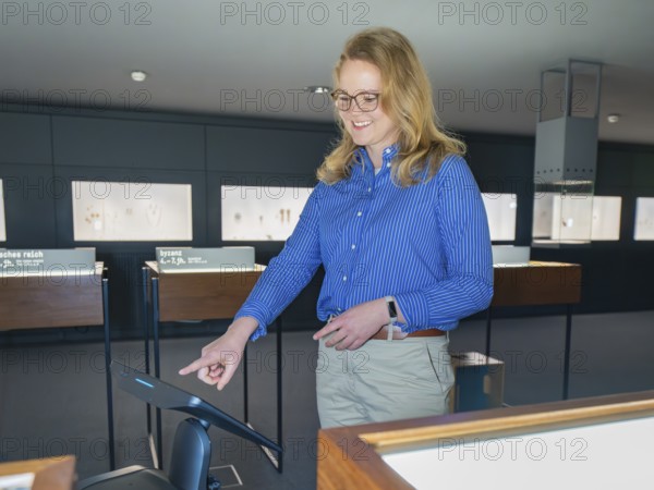 A woman in a blue shirt smiles and uses a digital screen in a museum, robotic personality Roboloutions in the jewelry museum, Pforzheim, Germany