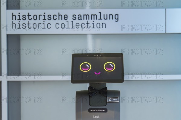 A cute robot with a smiley face in front of a sign with the inscription 'historical collection', robot personality Roboloutions in the jewelry museum, Pforzheim, Germany