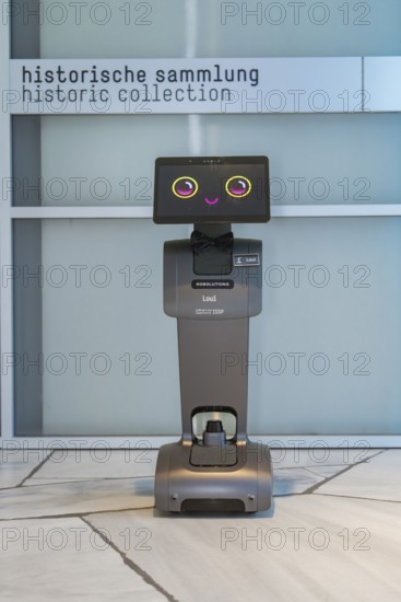 A robot stands in front of a sign for the historical collection on marble floor, robot personality Roboloutions in the jewelry museum, Pforzheim, Germany