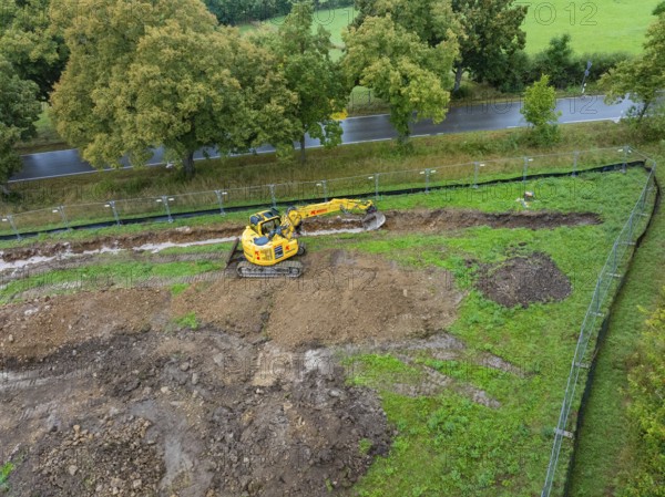 Excavator on a construction site with earthworks next to a road and trees, Bau PV Freifaechenanlage, Weil der Stadt, Germany