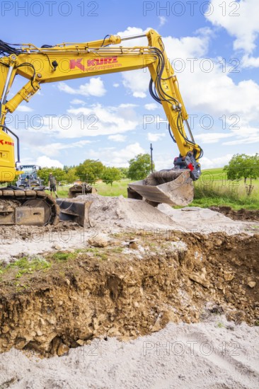 Excavator lifts soil on a construction site under a blue sky, Bau PV Freifaechenanlage, Weil der Stadt, Germany