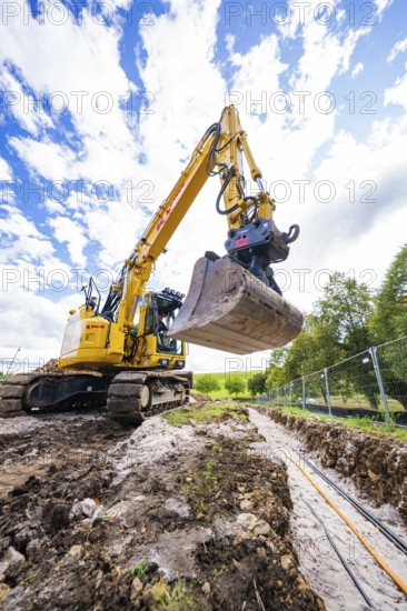 An excavator carries out earthworks on a construction site under a cloudy sky, Bau PV Freifaechenanlage, Weil der Stadt, Germany