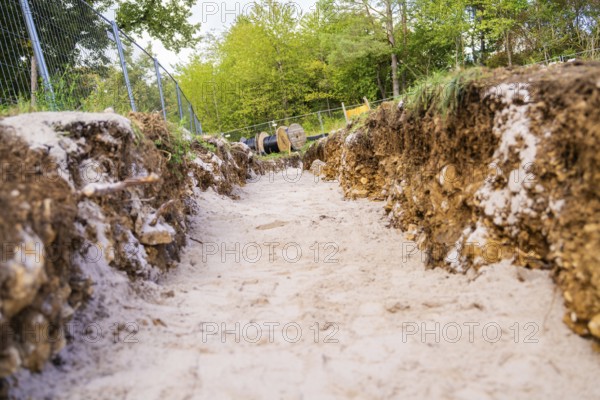 An excavated ditch with soil and sand on a construction site surrounded by vegetation, construction PV Freifaechenanlage, Weil der Stadt, Germany