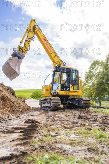 A yellow excavator picks up soil on a construction site under cloudy skies, Bau PV Freifaechenanlage, Weil der Stadt, Germany