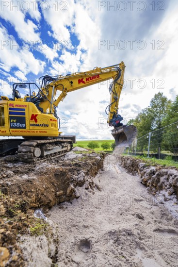 A yellow excavator carries out trenching work on a construction site under a cloudy sky, Bau PV Freifaechenanlage, Weil der Stadt, Germany