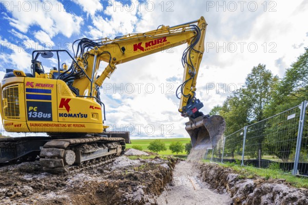 A yellow excavator digging on a construction site under a cloudy sky, Bau PV Freifaechenanlage, Weil der Stadt, Germany