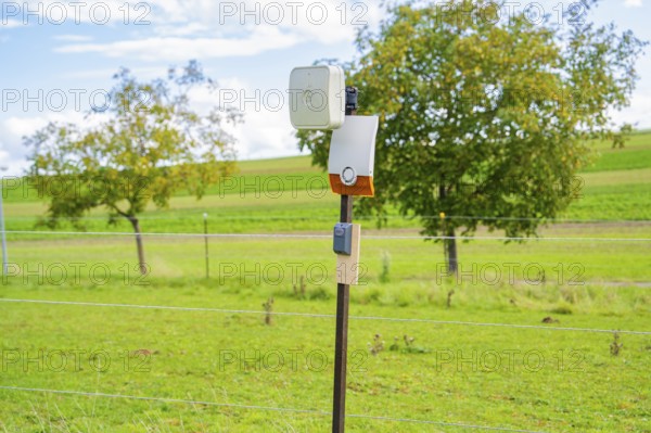 Camera on a post, surrounded by green fields and trees, against a cloudy sky, Bau PV Freifaechenanlage, Weil der Stadt, Germany