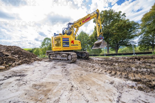 A construction machine moves soil on a construction site, surrounded by sky and trees, Bau PV Freifaechenanlage, Weil der Stadt, Germany
