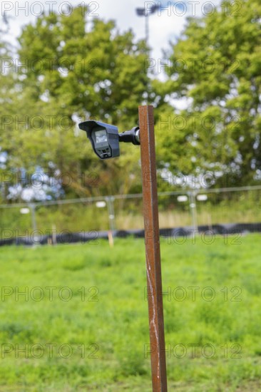 Camera on a tall post against green trees and a cloudy sky, Bau PV Freifaechenanlage, Weil der Stadt, Germany