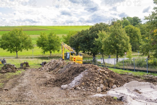 Excavator on a construction site with large mounds of soil in a green landscape, Bau PV Freifaechenanlage, Weil der Stadt, Germany