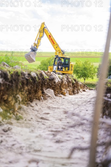 A yellow excavator works on a construction site on a mound under a blue sky, Bau PV Freifaechenanlage, Weil der Stadt, Germany
