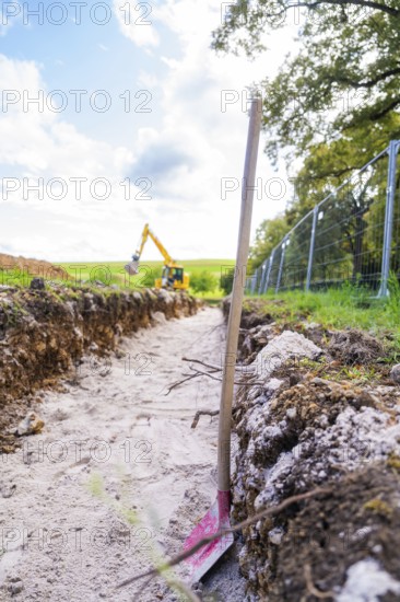 A ditch with an inserted shovel runs through a rural landscape under blue sky, Bau PV Freifaechenanlage, Weil der Stadt, Germany