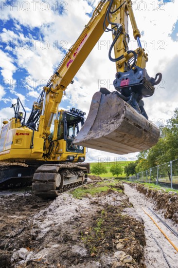 Large excavator digging a trench under cloudy sky, Bau PV Freifaechenanlage, Weil der Stadt, Germany
