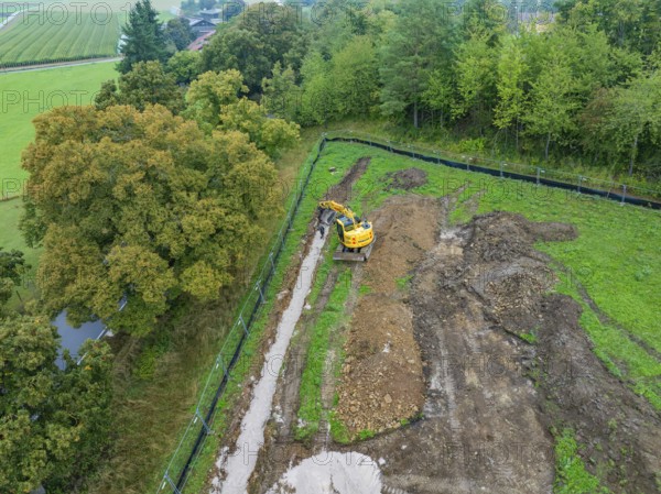 Excavator working on an earthen ditch in a green area, Bau PV Freifaechenanlage, Weil der Stadt, Germany
