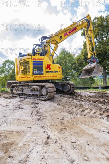 A yellow excavator doing earthwork on a construction site under cloudy skies, Bau PV Freifaechenanlage, Weil der Stadt, Germany