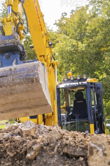 Close-up of an excavator with a raised grab arm at a construction site in front of trees, PV Freifaechenanlage construction, Weil der Stadt, Germany