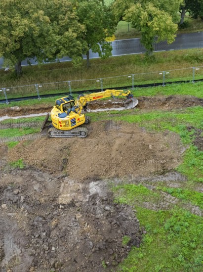 Excavator on a construction site with excavated soil surrounded by greenery and trees, Bau PV Freifaechenanlage, Weil der Stadt, Germany