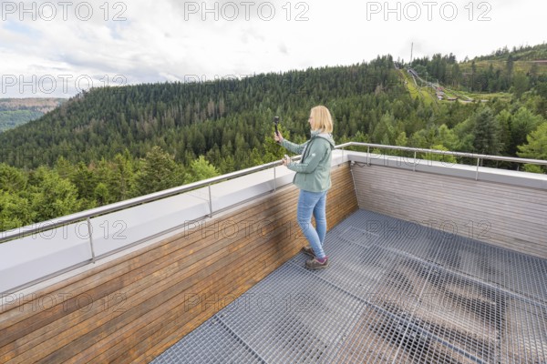 Individual taking photos of an elevated platform with a view of wooded hills, Ruhestein National Park Center, Black Forest, Baiersbronn, Germany