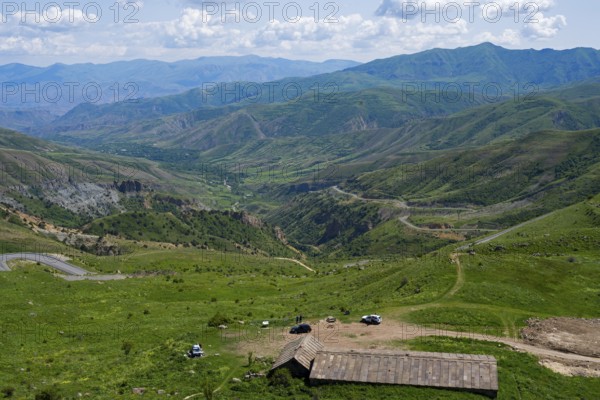 Mountains with isolated vehicles in a meadow, peaceful natural landscape under blue sky, view from Vardenyats Pass or Selim Pass, Vayots Dzor Province, Armenia