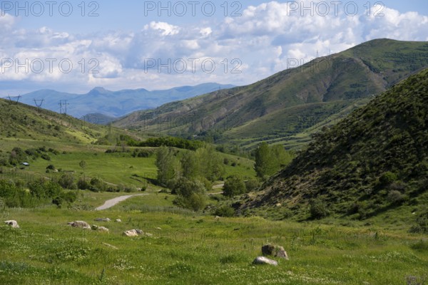 Mountainous valley with green meadow under a blue sky with clouds and power lines, landscape from south towards Vardenyats Pass or Selim Pass, Vayots Dzor province, Armenia