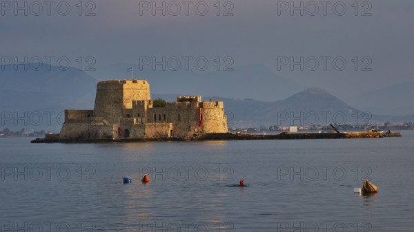 Bourtzi island fortress, old fortress on an island in the calm sea, surrounded by buoys and mountains in the evening light, Nauplion, Nafplion, Peloponnese, Greece