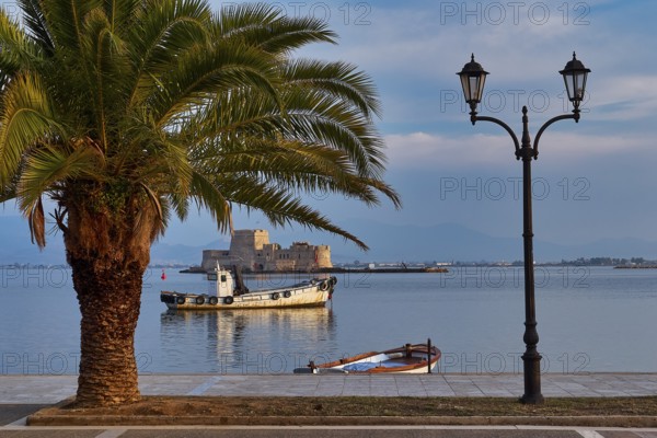 Bourtzi island fortress, port of Nauplion, palm tree and lanterns at the seaport with a view of a boat and a distant island, Nauplion, Nafplion, Peloponnese, Greece