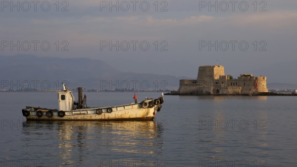Port of Nauplion, Bourtzi island fortress, A small boat in front of a historic fortress in the calm sea at dusk, Nauplion, Nafplion, Peloponnese, Greece