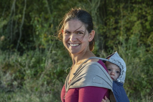 Young mother carrying her baby in a shawl on her back, Othenstorf, Mecklenburg-Western Pomerania, Germany