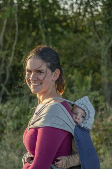 Young mother carrying her baby in a shawl on her back, Othenstorf, Mecklenburg-Western Pomerania, Germany