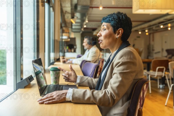 Professional businesswoman engaging in a video call and remote work, actively communicating with a headset and laptop from an office or coworking environment