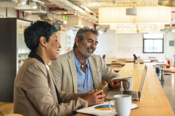 Diverse business colleagues are collaborating on a laptop, sharing ideas and discussing data in a bright coworking space, fostering teamwork and professional interaction