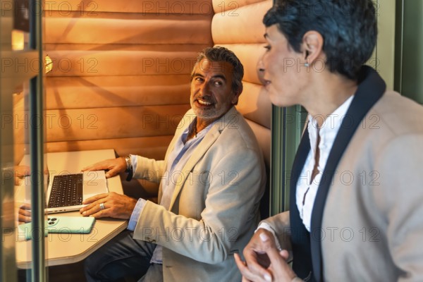Business colleagues having a relaxed discussion and working together in a cozy, soundproofed private cabin within a contemporary coworking office space
