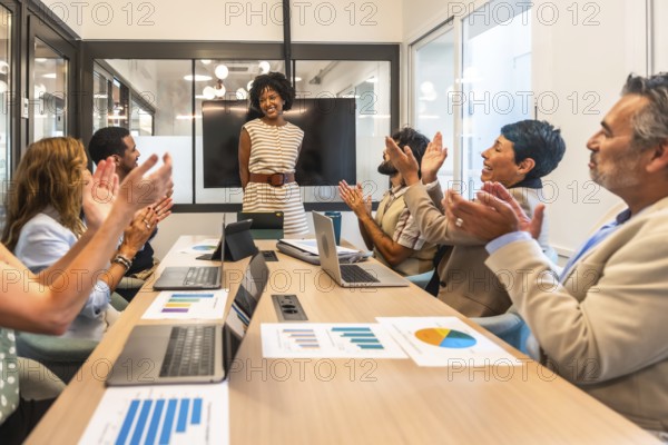 Diverse business professionals applaud a smiling female leader at a conference table after her successful presentation, celebrating achievement, teamwork and support in a modern office