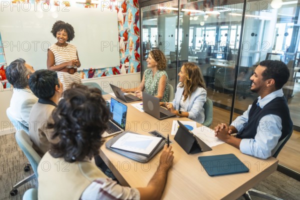 Diverse business colleagues actively participating in a positive meeting, listening to an african american presenter sharing ideas and strategies in a bright, modern office or coworking space